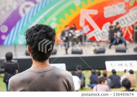 一個人正看著舞台,舞台上有一個大學生樂團在學校節慶上表演。 一個人正看著舞台,舞台上有一個大學生樂團在學校節慶上表演。 136493674