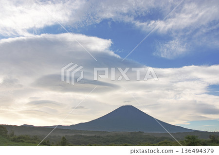 The beautiful, ultramarine Mount Fuji stands tall in the center of a cool summer plateau, with many hanging clouds floating in the sky. 136494379