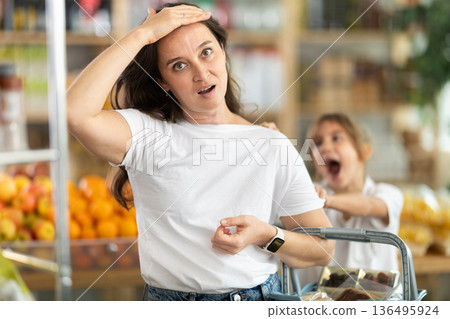 Capricious daughter screams and demands to buy sweets at the store. Mom is shocked by the naughty child 136495924