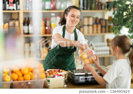 Woman sells fruits to girl, puts apples in bag, puts them on scale and weighs fruits Woman sells fruits to girl, puts apples in bag, puts them on scale and weighs fruits 136495925