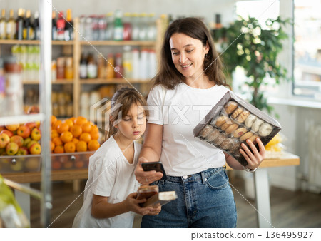Girl with mother customers at shop scans QR code on sweets package using phone camera 136495927