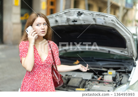 woman stands near a broken car with a phone in her hands 136495993