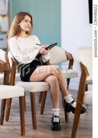 Portrait of diligent young female student listening and writing exercises on tablet at lesson in university 136496022