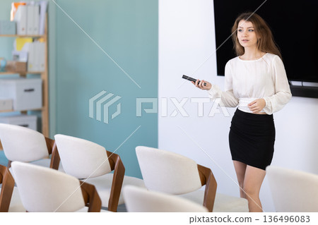 Young woman coach presenting in auditorium with remote control Young woman coach presenting in auditorium with remote control 136496083
