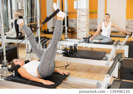 Girl performing legs exercise using straps on Pilates reformer 136496130