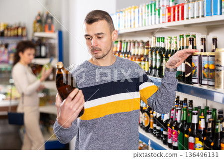Interested man making purchases in grocery store, buying bottle beer 136496131