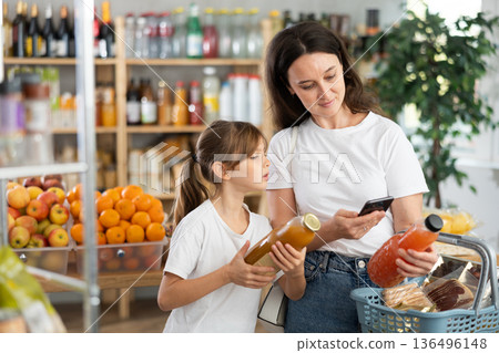 Mother and daughter choose bottles of juice and scan QR code with smartphone in supermarket Mother and daughter choose bottles of juice and scan QR code with smartphone in supermarket 136496148