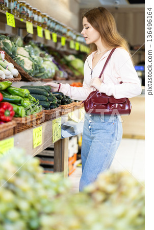 Girl selects ripe cucumers from counter in grocery store 136496164