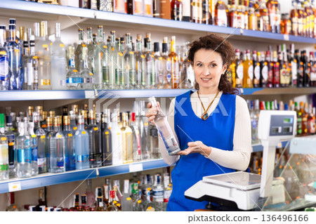Woman salesperson in alcohol department of Russian store stand with vodka near showcase. 136496166