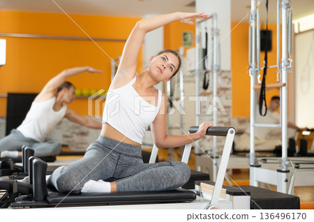 Girl doing side stretching with arm extended on Pilates reformer Girl doing side stretching with arm extended on Pilates reformer 136496170