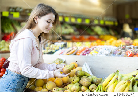 Young woman choosing a pear on the counter background Young woman choosing a pear on the counter background 136496174