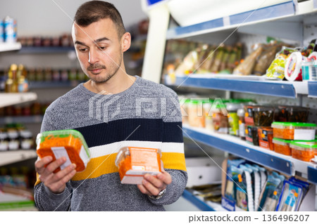 In Russian goods store, man choose package of pickled Korean spicy carrot salad 136496207
