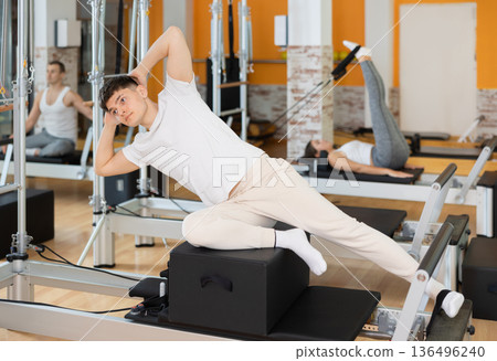 Man in different poses performs static and dynamic exercises on reformer Man in different poses performs static and dynamic exercises on reformer 136496240