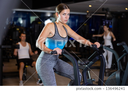 Sportive young girl doing air bike exercises in well-equipped gym 136496241