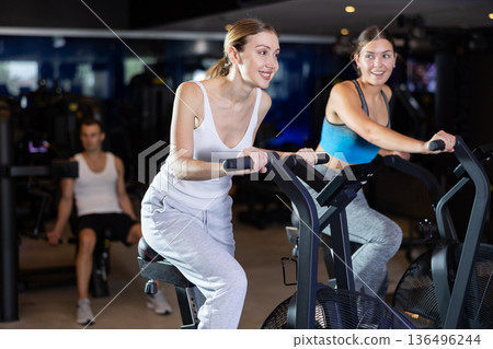 Sportive young girls doing air bike exercises in well-equipped gym Sportive young girls doing air bike exercises in well-equipped gym 136496244