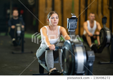 Determined young girl training with rowing machine in sports hall Determined young girl training with rowing machine in sports hall 136496272