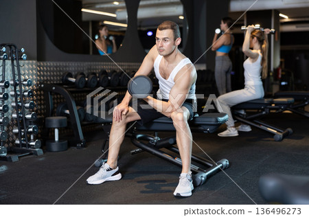 Man trains muscles of arms and back using dumb-bell shaped figure weighting. 136496273