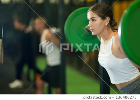 Sportive young woman lifting barbell in sports hall 136496275