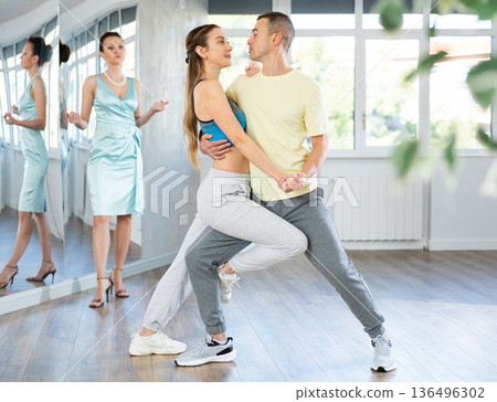 Couple in comfortable sports clothes learns tango dancing during individual lesson 136496302
