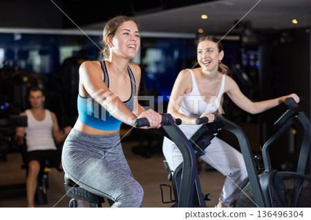 During classes on air bike, girls chat sweetly and smile 136496304
