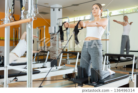 Girl performing pulling straps exercise on Pilates reformer Girl performing pulling straps exercise on Pilates reformer 136496314