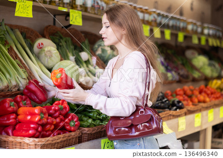 Girl selects ripe bell peppers from counter in grocery store Girl selects ripe bell peppers from counter in grocery store 136496340