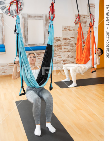 Man visitor performs exercises in hanging position on Pilates slings hammock Man visitor performs exercises in hanging position on Pilates slings hammock 136496341