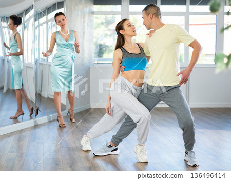Couple in comfortable sports clothes learns tango dancing during individual lesson Couple in comfortable sports clothes learns tango dancing during individual lesson 136496414
