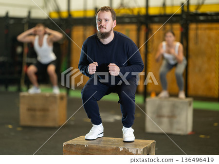 Bearded man performing jump-ups on box during high-intensity workout 136496419