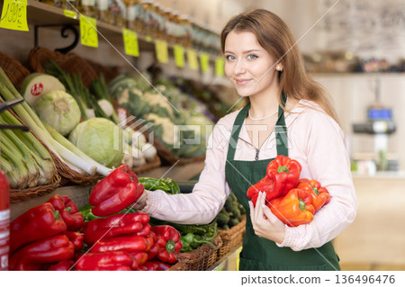 Woman employees in uniform holding fresh bell pepper in grocery shop Woman employees in uniform holding fresh bell pepper in grocery shop 136496476