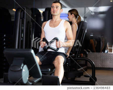 Sportive young guy training his arms using cable exercise machine in gym Sportive young guy training his arms using cable exercise machine in gym 136496483