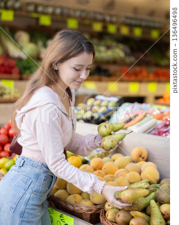 Woman chooses pears for purchase in greengrocer shop Woman chooses pears for purchase in greengrocer shop 136496498