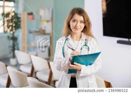 Young female doctor with folder invites in lecture hall Young female doctor with folder invites in lecture hall 136496522