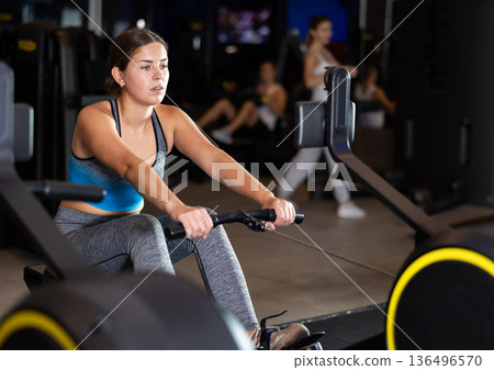 Girl performs exercises with rowing machine in gym Girl performs exercises with rowing machine in gym 136496570