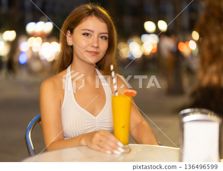 Woman sits at a table in a cafe overlooking the evening city of Barcelona 136496599