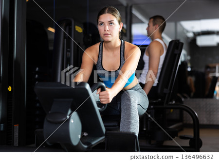 Girl pulls handle of simulator with effort during strength training Girl pulls handle of simulator with effort during strength training 136496632