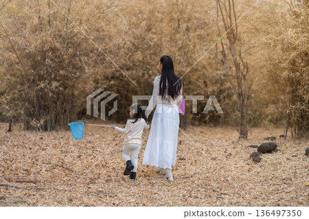 Mother and child girl walking in a dry field with colorful butterfly nets in forest. Mother and child girl walking in a dry field with colorful butterfly nets in forest. 136497350