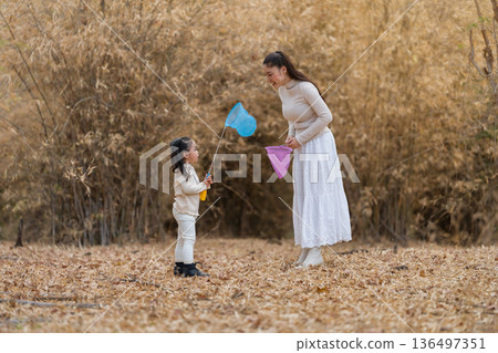 Mother and child girl bonding while playing with butterfly nets in dry forest. 136497351