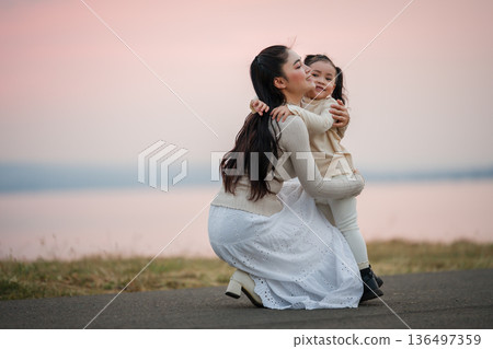 Heartwarming moment of mother and daughter hugging by lakeside at sunset 136497359