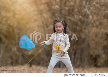 Little child girl holding blue butterfly net exploring the dry forest 136497407