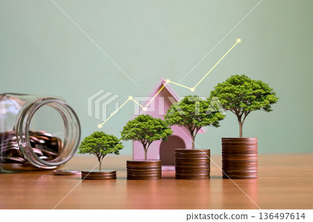 Financial growth and real estate investment concept featuring money trees on rising coin stacks, a house model, and an upward trending graph. Ideal for wealth management, savings, retirement planning, 136497614
