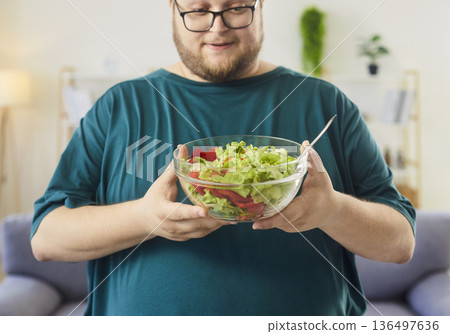 Man with glasses looking at fresh salad bowl filled with lettuce and veggies 136497636