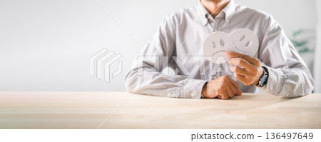 Man holding happy and sad face cutouts displays emotional contrast for customer feedback survey, reflecting diverse moods, evaluating health or service quality for business satisfaction Man holding happy and sad face cutouts displays emotional contrast for customer feedback survey, reflecting diverse moods, evaluating health or service quality for business satisfaction 136497649