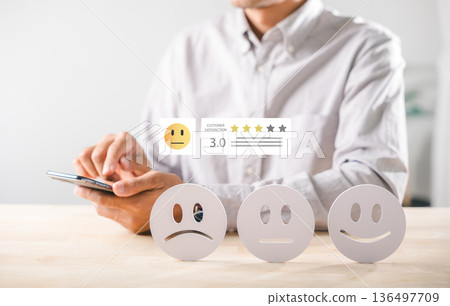 Satisfaction customer review survey highlights online feedback experience, mobile phone user rates service 3 stars, displaying neutral emoji choice and physical emotion icons on table Satisfaction customer review survey highlights online feedback experience, mobile phone user rates service 3 stars, displaying neutral emoji choice and physical emotion icons on table 136497709