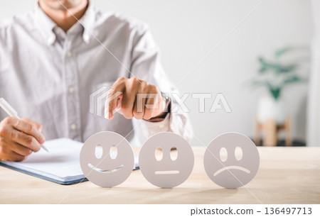 Survey on customer satisfaction, person hand points to happy face emoticon for review, writing service feedback on form, evaluating positive customer experience on desk Survey on customer satisfaction, person hand points to happy face emoticon for review, writing service feedback on form, evaluating positive customer experience on desk 136497713