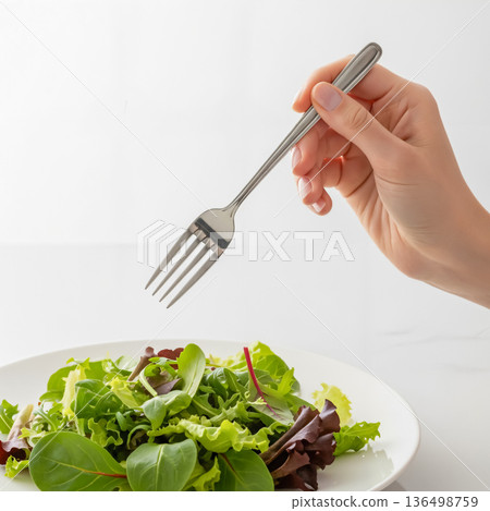 Close-up of a hand holding a fork and eating salad 136498759