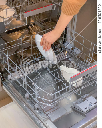 A woman's hand puts dirty dishes in the dishwasher 136501230