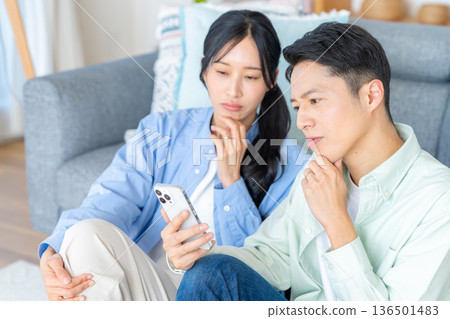 夫婦在客廳裡看智能手機 夫婦在客廳裡看智能手機 136501483