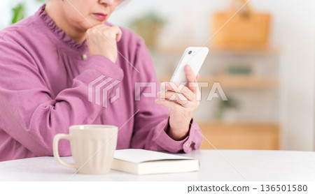 一位神情焦慮的老婦人正看著她的智慧型手機（詐騙、麻煩、擔憂） 136501580