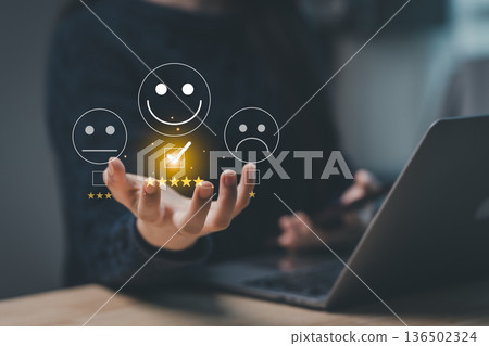 Hand holding smiling and sad emoticons with checkmark symbol, representing customer satisfaction and feedback concept in digital communication setting Hand holding smiling and sad emoticons with checkmark symbol, representing customer satisfaction and feedback concept in digital communication setting 136502324